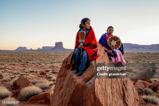 夜明けの砂漠の驚くべきミトン岩の形成の前で赤い岩の上にポーズをとるモニュメントバレーの若いナバホ兄弟と姉妹 - ute ストックフォトと画像