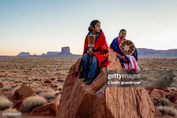 young navajo brother and sister in monument valley posing on red rocks in front of the amazing mittens rock formations in the desert at dawn - cherokee stock pictures, royalty-free photos & images