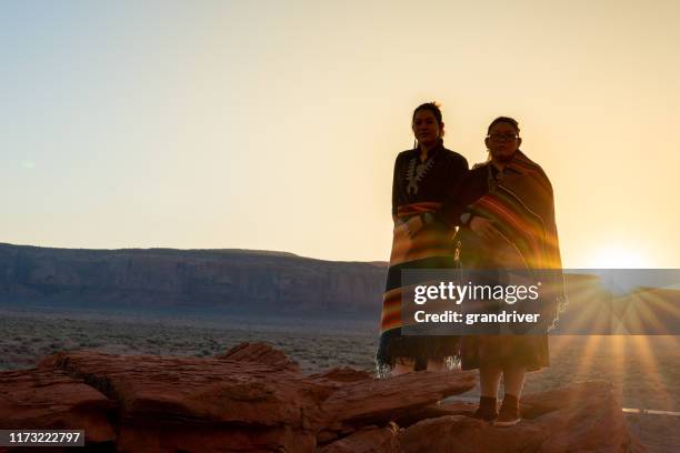 twee tiener native american indian navajo zuster in traditionele kleding genieten van de uitgestrekte woestijn en rode rots landschap in de beroemde navajo tribal park in monument valley arizona bij dawn - cherokee indian women stockfoto's en -beelden