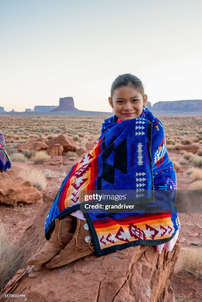 Ganska nio år gamla infödda amerikanska Navajo indisk flicka i de tidiga morgontimmarna klädd i traditionella kläder poserar framför Monument Valley Tribal Park