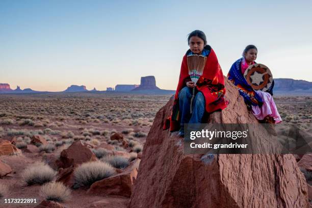 jonge navajo broer en zus in monument valley poseren op rode rotsen in de voorkant van de verbazingwekkende wanten rotsformaties in de woestijn bij dageraad - indianenreservaat stockfoto's en -beelden