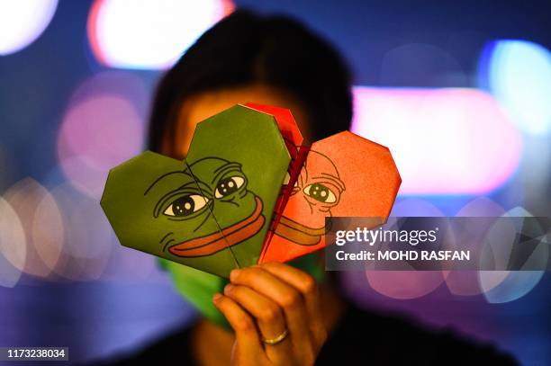 This picture taken on September 30, 2019 shows a protester holding origami hearts with a depiction of Pepe the Frog, a character used by...