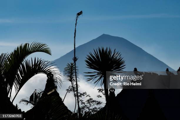 View of Mt Agung volcano on Bali from just below Penelokan on the road to Tampaksiring with silhouettes of palms and temple roofs in the foreground.