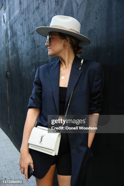 Guest poses wearing a hat, black top and black bottoms and black blazer with a white Yves St Laurent purse outside the Jason Wu show during New York...