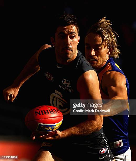 Kade Simpson of the Blues handballs under pressure from Mark Nicoski of the Eagles during the round 14 AFL match between the Carlton Blues and the...