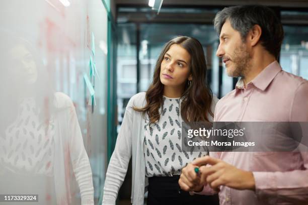 coworkers discussing over whiteboard in office - woman whiteboard stock pictures, royalty-free photos & images
