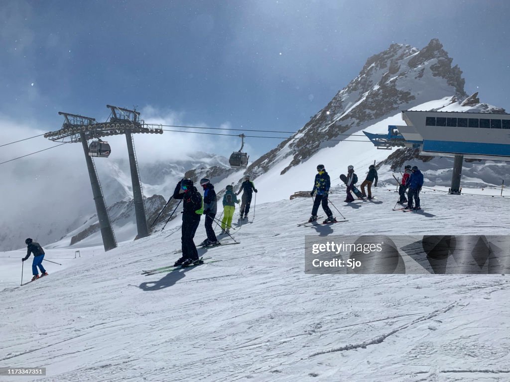 People preparing to ski and snowboard down a ski slope in the Sölden Ötztal ski area in the Austrian Alps during a sunny winter day.