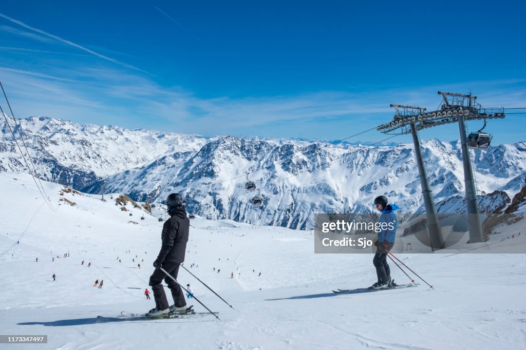 Människor som förbereder sig för att åka skidor och snowboard nedför en skidbacke i skidområdet Sölden Ötztal i de österrikiska Alperna under en solig vinterdag.