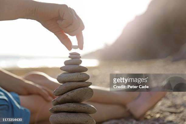 woman stacking stones on beach - pebbles stockfoto's en -beelden