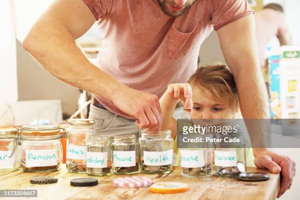young girl and father putting money into savings jars - budget stockfoto's en -beelden