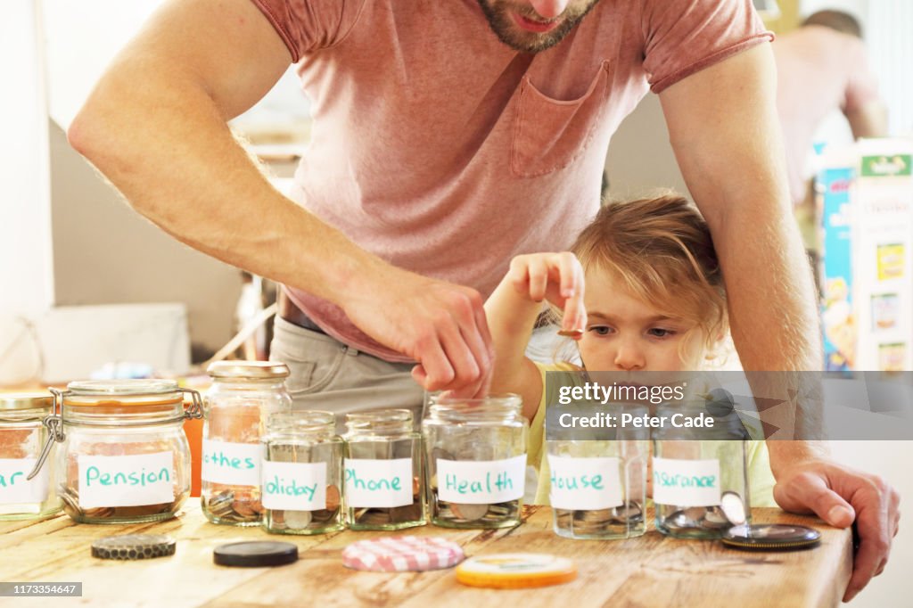 Young girl and father putting money into savings jars