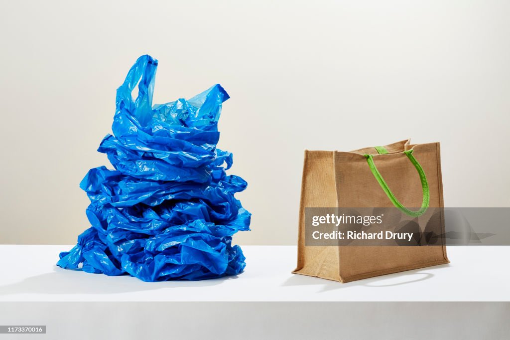 A stack of plastic carrier bags next to a reusable shopping bag