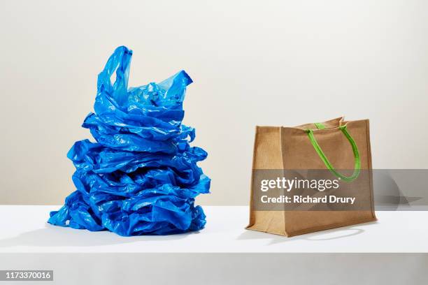 a stack of plastic carrier bags next to a reusable shopping bag - reusable bag fotografías e imágenes de stock