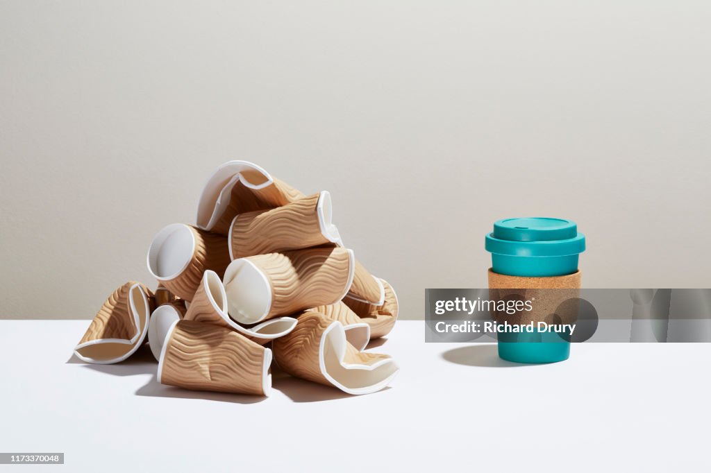 A pile of disposable coffee cups next to a reusable coffee cup