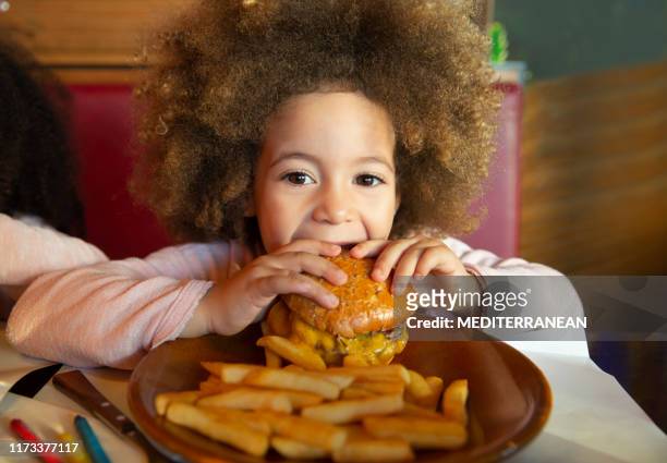 ethnic kid girl eating burger and chips - burger restaurant stock pictures, royalty-free photos & images