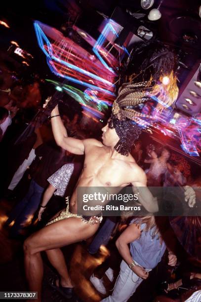 An unidentified man, dressed only in a feathered headdress and bikini briefs dances with a pair of paper fans on the floor at the Copacabana...