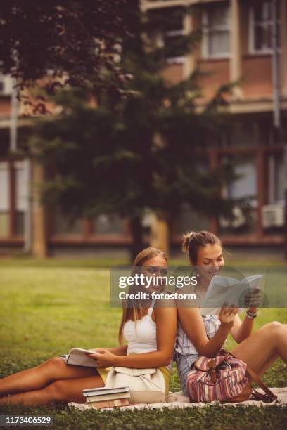 jeunes filles s'asseyant dans un stationnement, lisant - fille lire gazon photos et images de collection