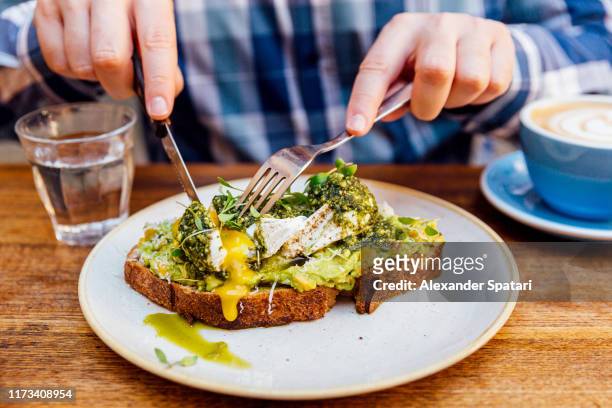 man eating avocado toast with poached egg, close up - cutting avocado stockfoto's en -beelden