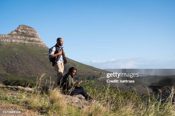 man standing by girlfriend sitting on cliff - lion's head mountain stock pictures, royalty-free photos & images