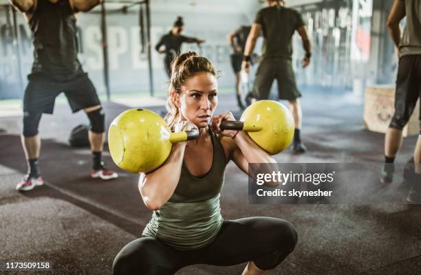 vastberaden atletische vrouw trainen met ketel klokken in een sportschool vol met mensen. - kettle bells stockfoto's en -beelden