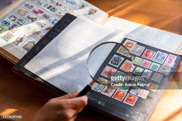 hands of a philatelist with a magnifier on a background of a stamp album - stamp collection stock pictures, royalty-free photos & images