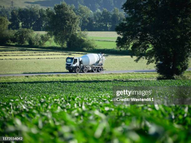 cement truck moving on highway along green field - betonmischmaschine stock-fotos und bilder