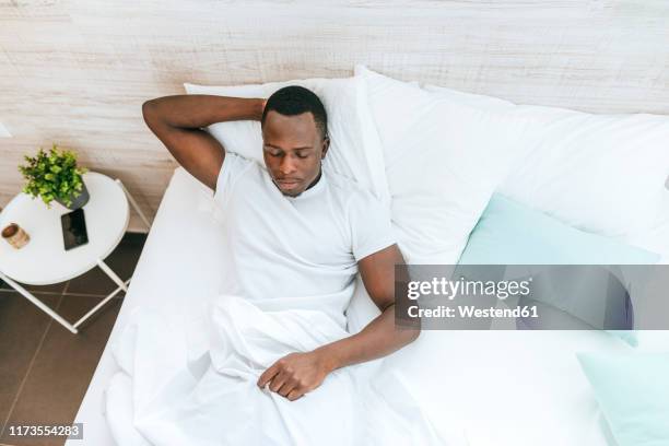 young man lying in bed at home - black man sleeping in bed stock pictures, royalty-free photos & images