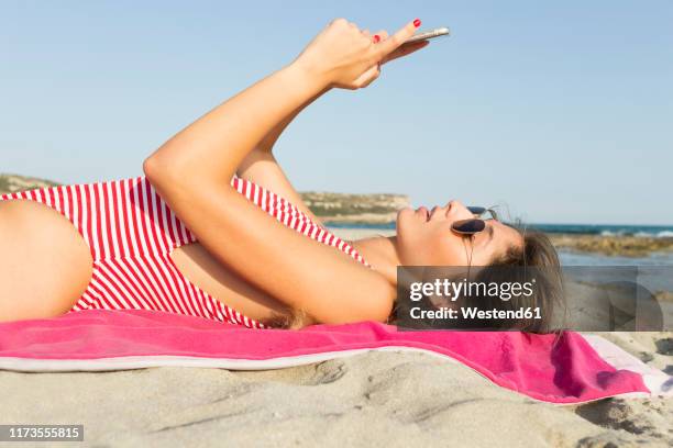 young woman using smartphone on the beach - woman towel beach stock-fotos und bilder