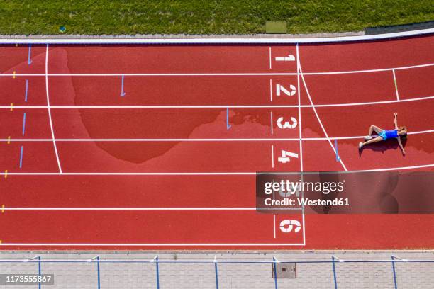 aerial view of a young female athlete lying on a tartan track after crossing the finishing line - tartanbahn stock-fotos und bilder