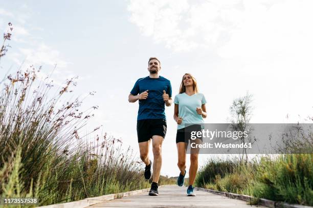 young couple jogging on wooden walkway - couple running stock pictures, royalty-free photos & images