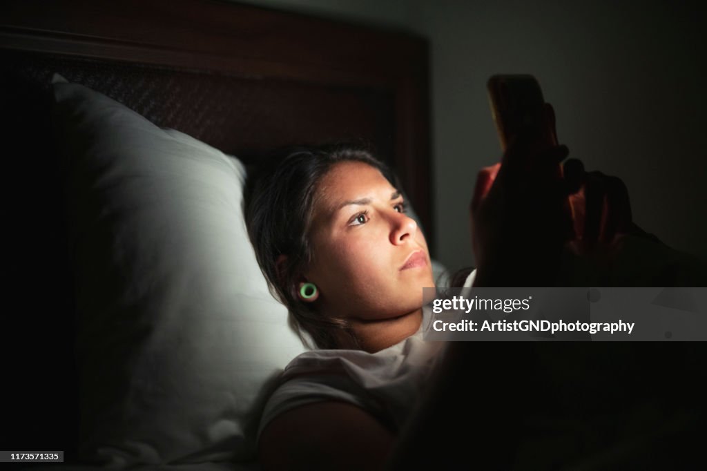 Young woman laying in bed and using smart phone.