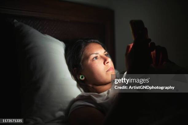 young woman laying in bed and using smart phone. - vice after dark stock pictures, royalty-free photos & images