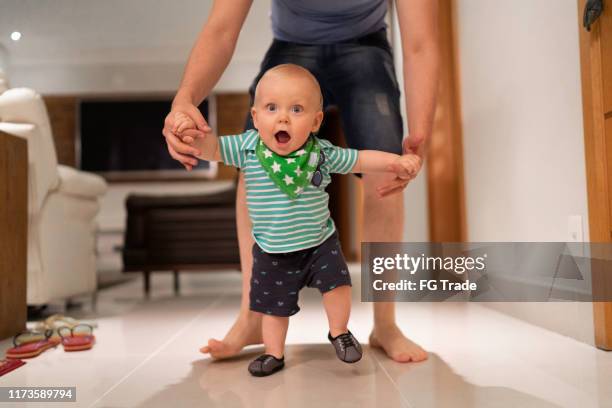 père aidant le fils apprennent à marcher à la maison - bébé rire photos et images de collection