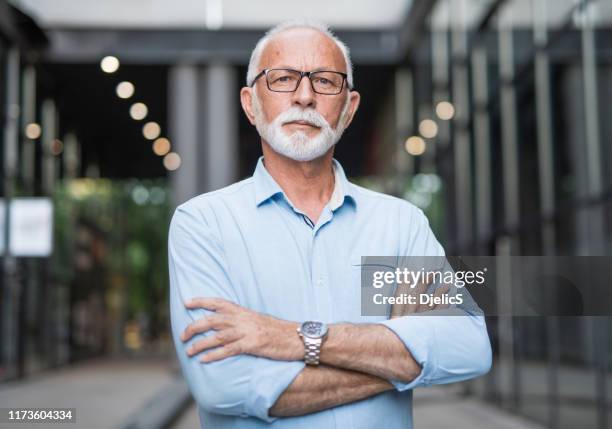 entrepreneur aîné restant à l'extérieur à côté des immeubles de bureaux et regardant l'appareil-photo. - homme 60 ans portrait photos et images de collection