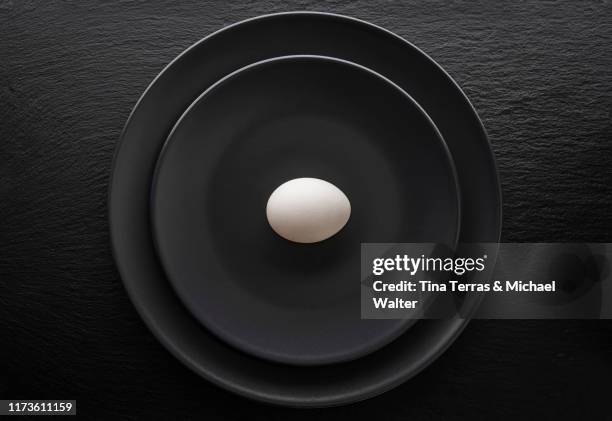 an egg on a black plate. the plate is standing on a black slate plate. - black plate stock pictures, royalty-free photos & images