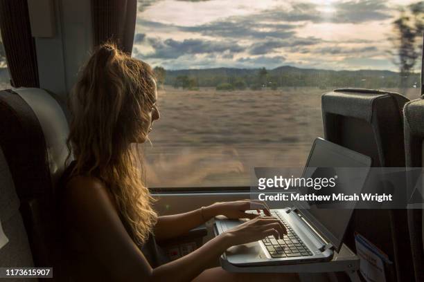 a woman works on her laptop while traveling on a train. - passenger stock pictures, royalty-free photos & images