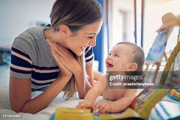 mutter spielt mit ihrem kleinen baby auf dem bett - mutter kind lachen zuhause stock-fotos und bilder