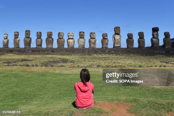 Woman gazes at Moais on ceremonial platform Ahu Tongariki at Rapa Nui National Park, in the southwest of Island. Moais are monolithic human figures...