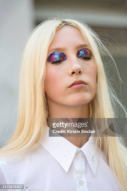 Model Sasha Komarova wears a white shirt dress and has shiny rainbow eyeshadow on July 03, 2019 in Paris, France.
