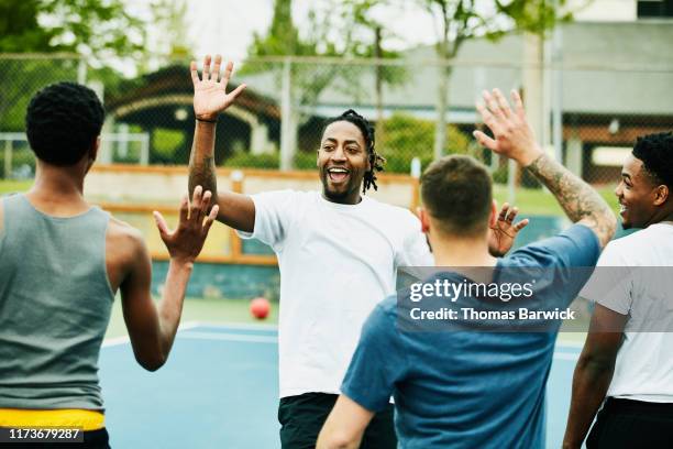 smiling man high fiving teammates after winning dodgeball game - team t shirt imagens e fotografias de stock