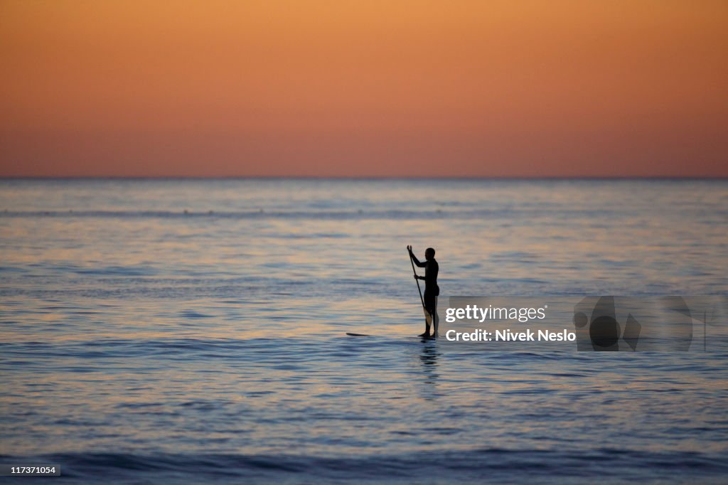 Lone stand-up paddle board surfer at sunset