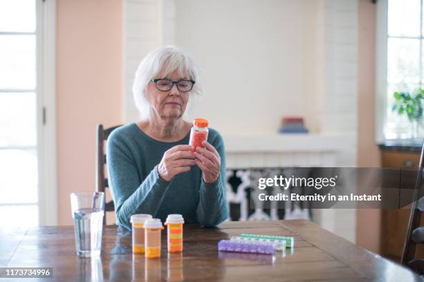 senior woman reading her medicine bottle - taking medication stockfoto's en -beelden