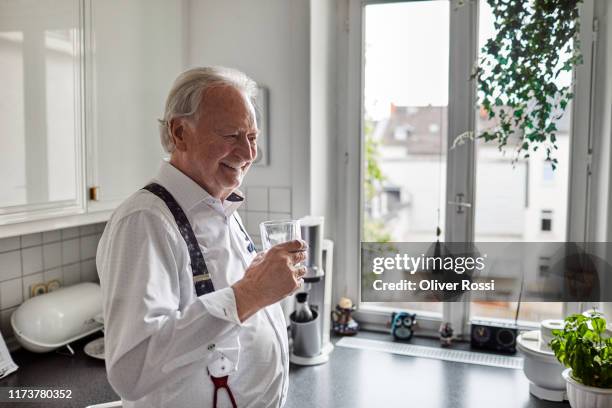 smiling senior man in kitchen at home drinking glass of water - wasser trinken zu hause stock-fotos und bilder