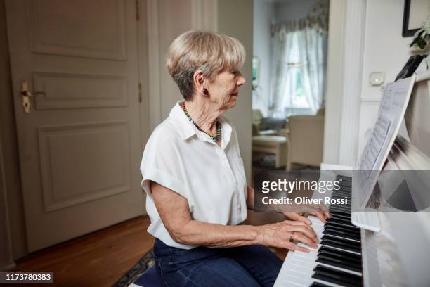 senior woman playing piano at home - pianist stock pictures, royalty-free photos & images