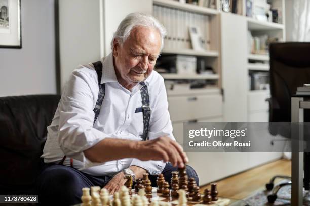 senior man sitting on couch playing chess at home - senior playing chess stock pictures, royalty-free photos & images