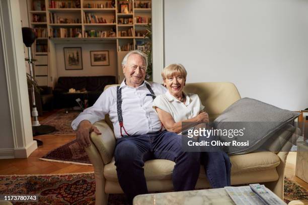 portrait of smiling senior couple sitting on couch at home - ehemann stock-fotos und bilder