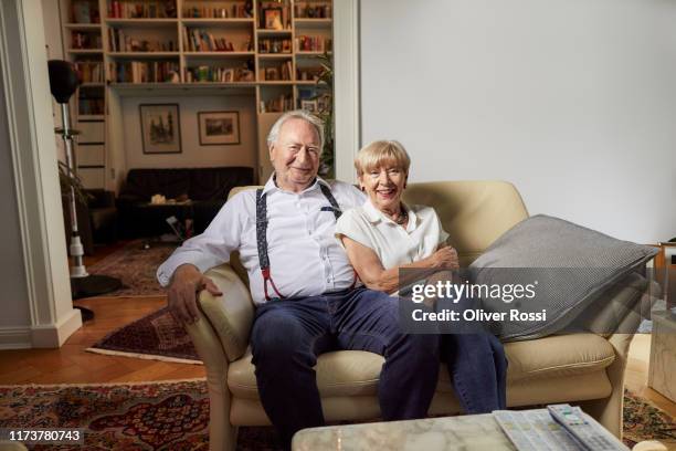 portrait of smiling senior couple sitting on couch at home - married imagens e fotografias de stock