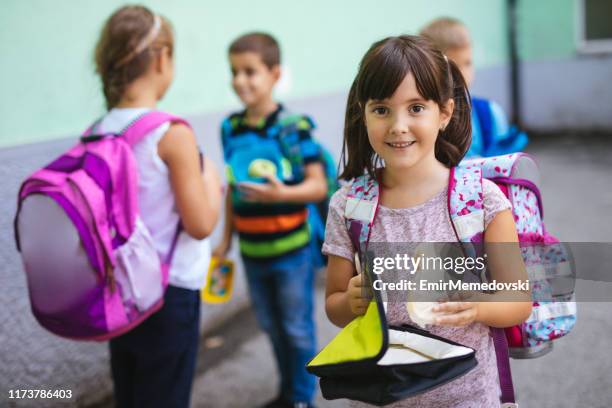 little girl holding lunch box and eating sandwich in a school yard - boy packlunch stock pictures, royalty-free photos & images