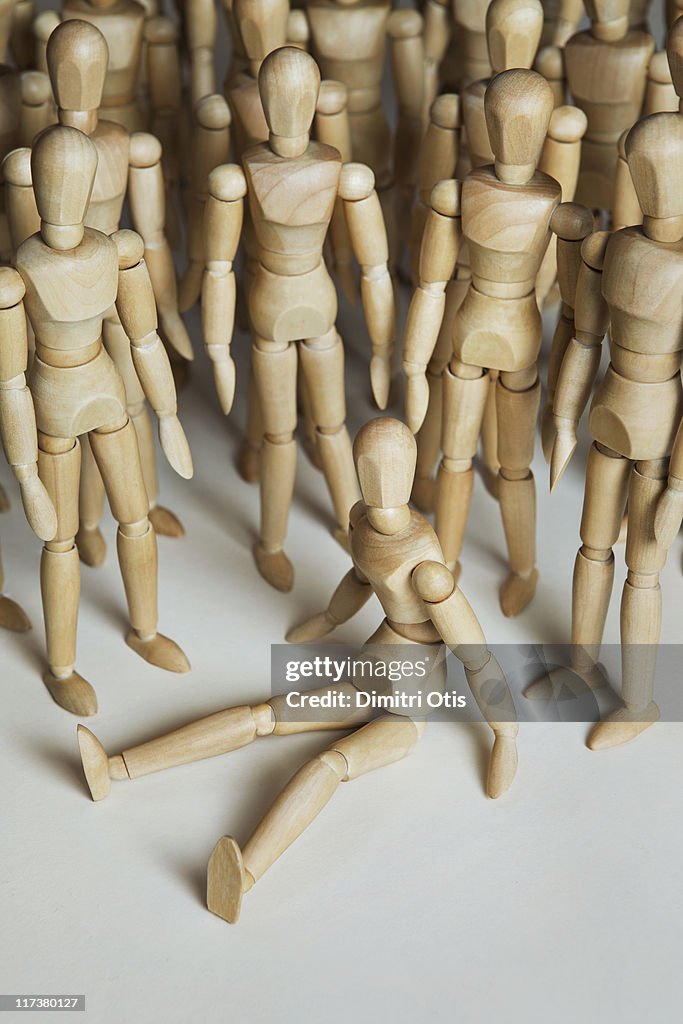 A wood mannequin sitting with many others standing