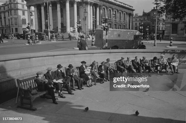 Wartime view of Londoners sitting on benches reading newspapers in Trafalgar Square, with St Martin-in-the-Fields church in the background, during...